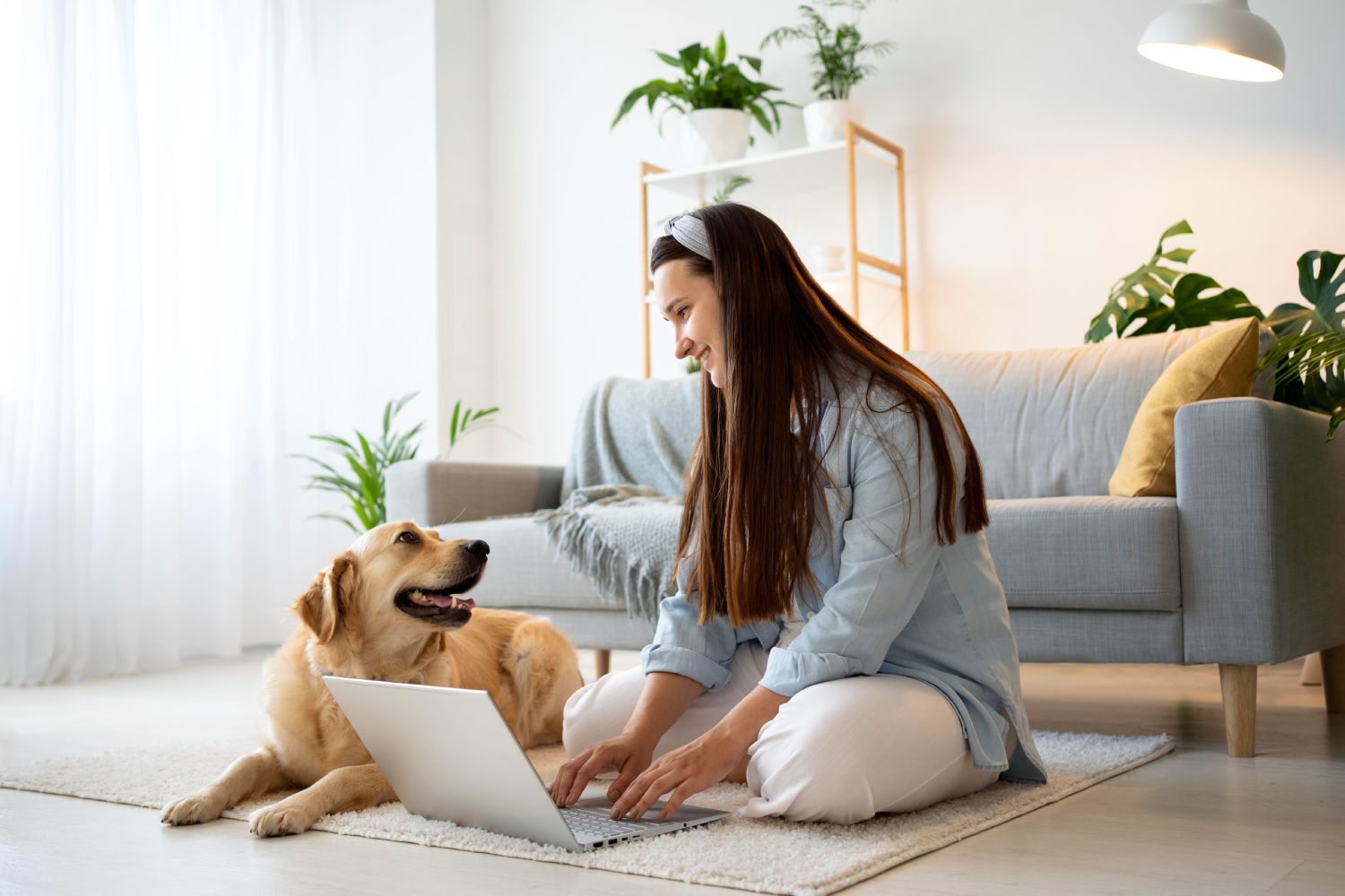 Den Mieter:innen Haustiere in der Wohnung erlauben? Eine Frau, die mit ihrem Hund und einem Laptop im Wohnzimmer auf dem Boden sitzt.