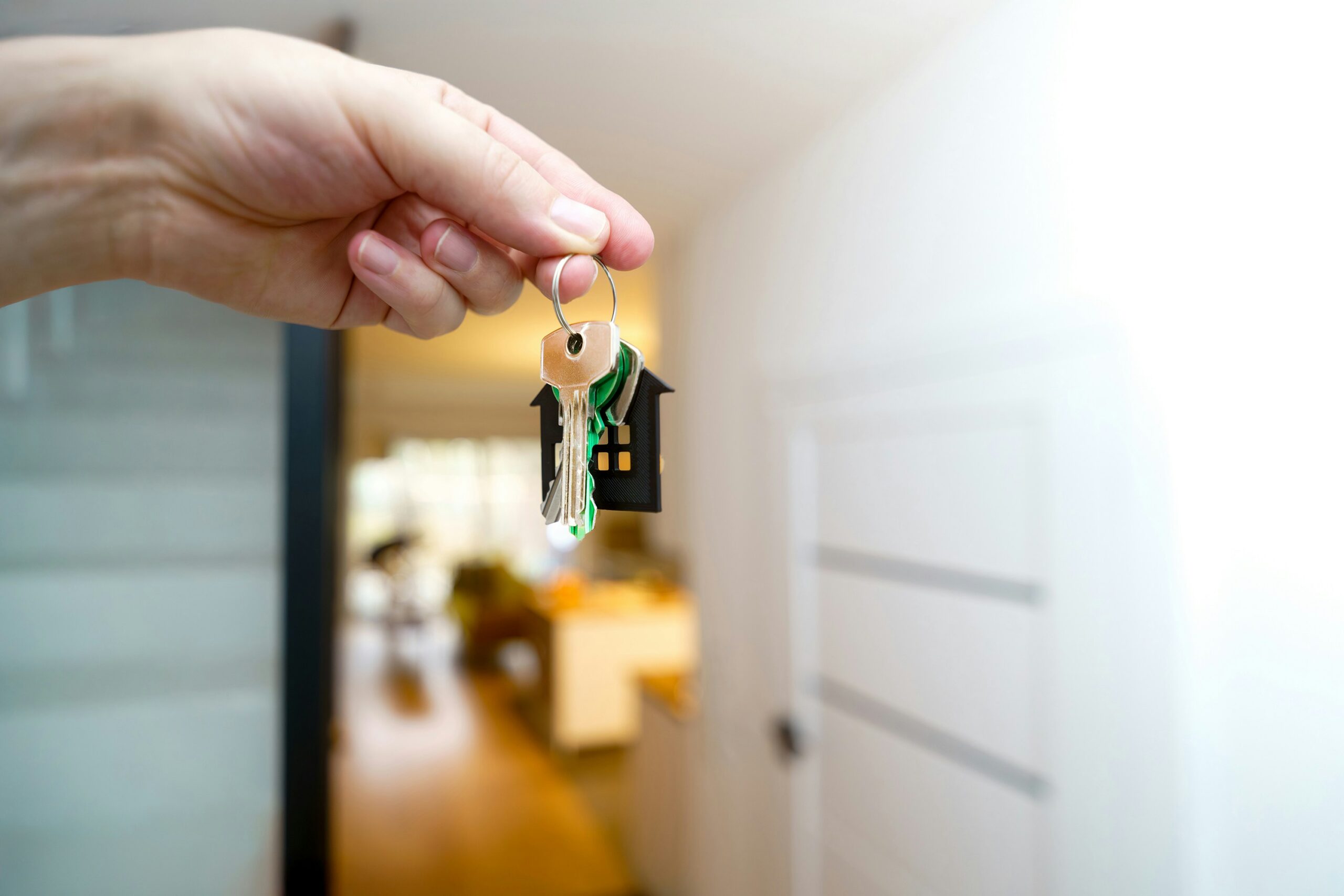 Hand holding a keyring with several metal keys and a small house-shaped keychain in focus.