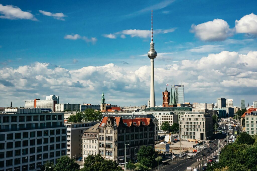 Berlin skyline featuring the Fernsehturm TV tower against a blue sky with scattered clouds and surrounding buildings.