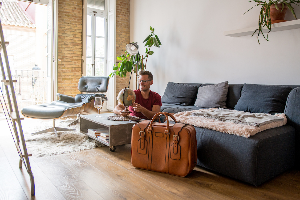 Moving to Paris: a man with a packed suitcase sitting in a living room, happily exploring a globe.